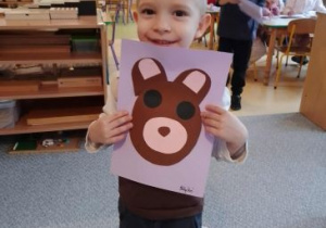 Kajtuś pozuje do zdjęcia trzymając w ręku pracę plastyczną