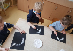 Dzieci stemplują karton białą farbą z wykorzystaniem widelca