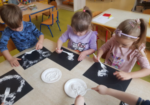 Dzieci stemplują karton białą farbą z wykorzystaniem widelca