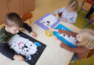 Dzieci stemplują śnieg na kartonie, korzystając z patyczków higienicznych