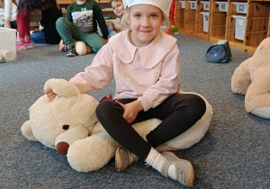 Dziewczynka z papierową koroną na głowie siedzi na dużym pluszowym misiu