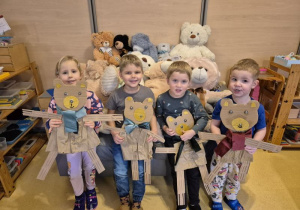 Dzieci pozują do zdjęcia z wykonanymi przez siebie misiami z kartonów, w tle pluszowe misie