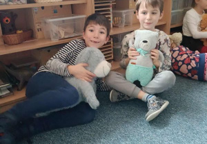 Dwóch chłopców siedzi na dywanie i trzymają w dłoniach pluszowe misie