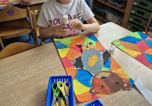 Dziewczynka przykleja narysowanego i wyciętego misia na kolorowe tło