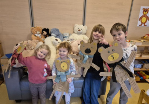 Dzieci pozują do zdjęcia z wykonanymi przez siebie misiami z kartonów, w tle pluszowe misie