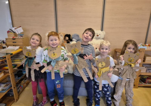Dzieci pozują do zdjęcia z wykonanymi przez siebie misiami z kartonów, w tle pluszowe misie