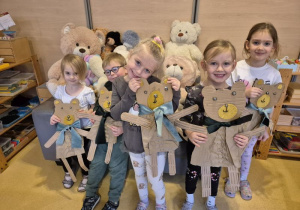 Dzieci pozują do zdjęcia z wykonanymi przez siebie misiami z kartonów, w tle pluszowe misie