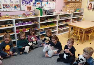 Dzieci siedzą na dywanie ze swoimi pluszakami