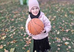 Tosia pozuje do zdjęcia trzymając piłkę do koszykówki w dłoniach