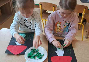 Dziewczynki dorysowują trawę na swojej pracy plastycznej przy użyciu zielonych pasteli