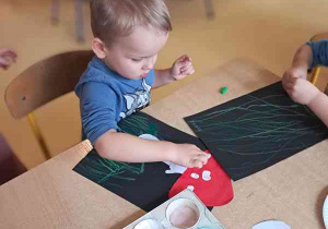 Chłopiec stempluje białe kropki palcem zamoczonym w farbie