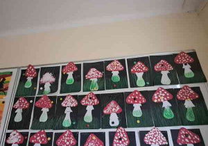 Wystawa prac dzieci przedstawiających muchomory utworzona na tablicy w szatni przedszkola
