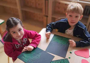 Dzieci w czasie wykonywania pracy plastycznej kreślą zielone linie na czarnym tle