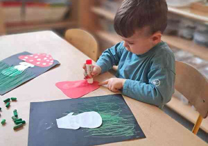 Chłopiec podczas wykonywania pracy plastycznej smaruje klejem element kolorowego papieru