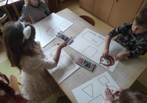 Dzieci kolorują kredkami figury geometryczne.