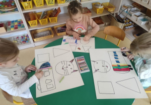 Dzieci kolorują kredkami figury geometryczne.