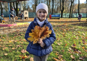 Dziewczynka stoi z bukietem liści w ogrodzie