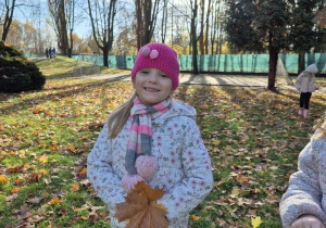 Dziewczynka stoi z bukietem liści w ogrodzie