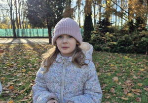 Dziewczynka stoi z kasztanami w dłoniach w ogrodzie