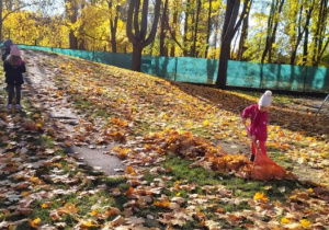 Dziewczynka grabi liście, dzieci wchodzą na górkę