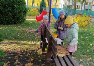 Dziewczynki bawią się w ogrodzie i układają liście na ławce