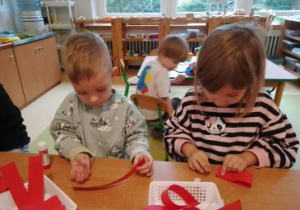 Kajtek i Liwia sklejają czerwone paski papieru