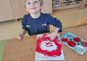 Franio tworzy pracę plastyczną wykorzystując gąbkę namoczoną w czerwonej farbie