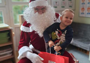 Chłopiec pozuje do zdjęcia z Mikołajem i prezentem