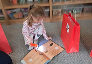 Dziewczynka siedzi na dywanie ogląda prezenty od Mikołaja