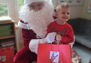 Chłopiec pozuje do zdjęcia z Mikołajem i prezentem