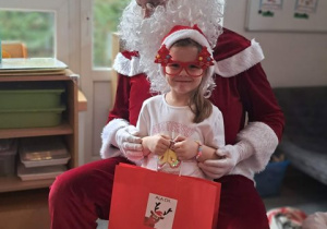 Dziewczynka pozuje do zdjęcia z Mikołajem i prezentem
