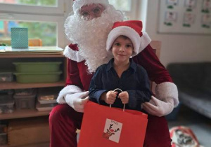 Chłopiec pozuje do zdjęcia z Mikołajem i prezentem