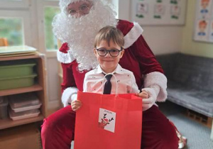 Chłopiec pozuje do zdjęcia z Mikołajem i prezentem