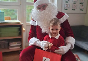 Chłopiec pozuje do zdjęcia z Mikołajem i prezentem