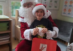 Chłopiec pozuje do zdjęcia z Mikołajem i prezentem