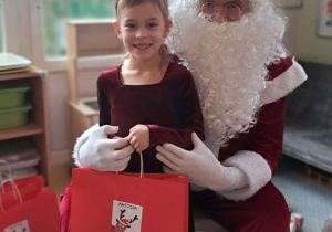 Dziewczynka pozuje do zdjęcia z Mikołajem i prezentem