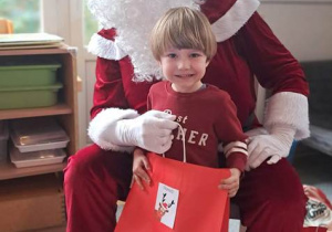 Chłopiec pozuje do zdjęcia z Mikołajem i prezentem