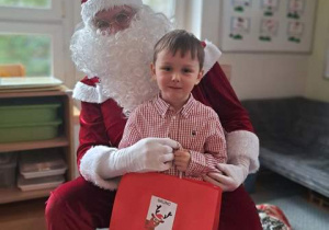 Chłopiec pozuje do zdjęcia z Mikołajem i prezentem