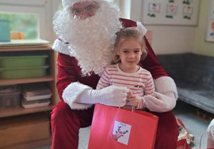 Dziewczynka pozuje do zdjęcia z Mikołajem i prezentem