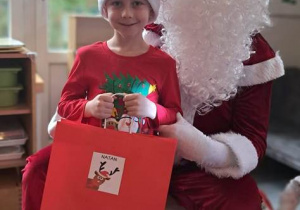Chłopiec pozuje do zdjęcia z Mikołajem i prezentem