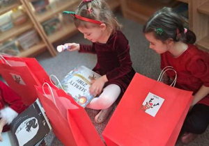 Dziewczynki siedzą na dywanie i rozpakowują prezenty od Mikołaja