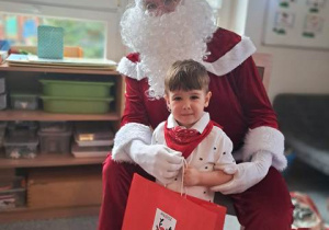 Chłopiec pozuje do zdjęcia z Mikołajem i prezentem