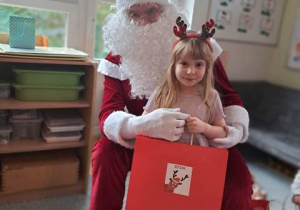 Dziewczynka pozuje do zdjęcia z Mikołajem i prezentem