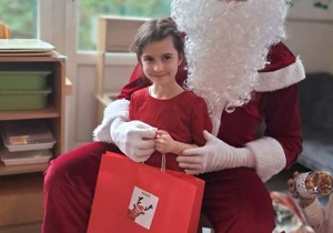 Dziewczynka pozuje do zdjęcia z Mikołajem i prezentem