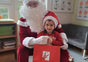 Chłopiec pozuje do zdjęcia z Mikołajem i prezentem