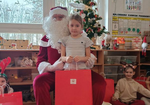 Dziewczynka pozuje do zdjęcia z Mikołajem i prezentem