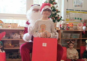 Chłopiec pozuje do zdjęcia z Mikołajem i prezentem