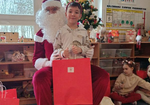 Chłopiec pozuje do zdjęcia z Mikołajem i prezentem