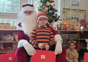 Chłopiec pozuje do zdjęcia z Mikołajem i prezentem