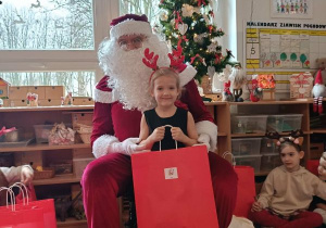 Dziewczynka pozuje do zdjęcia z Mikołajem i prezentem
